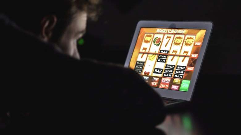 Gambling addicted man with glasses in front of online casino slot machine on laptop computer at night